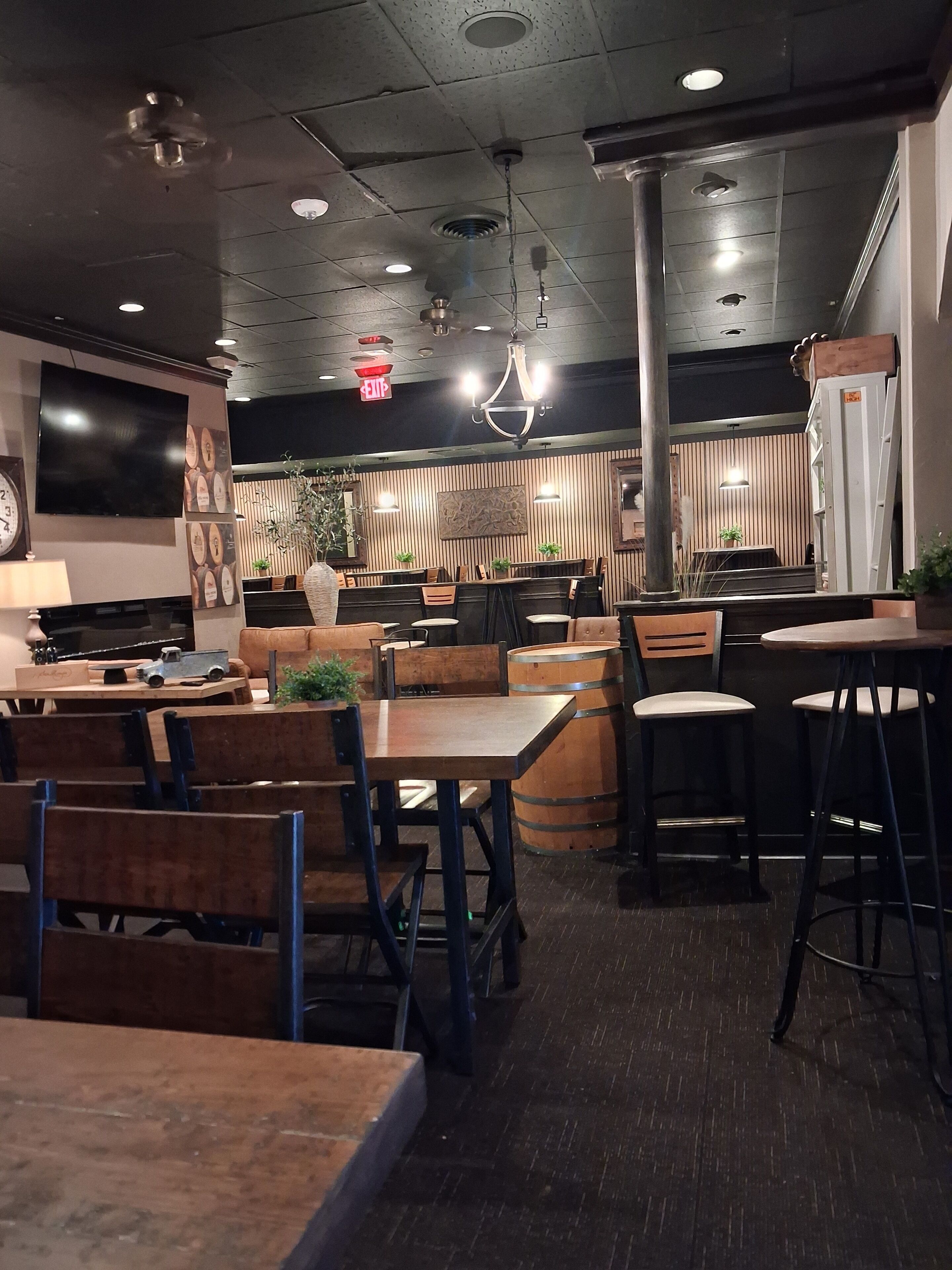 Interior de un restaurante con mesas y sillas de madera, un televisor montado en la pared e iluminación empotrada en el techo.