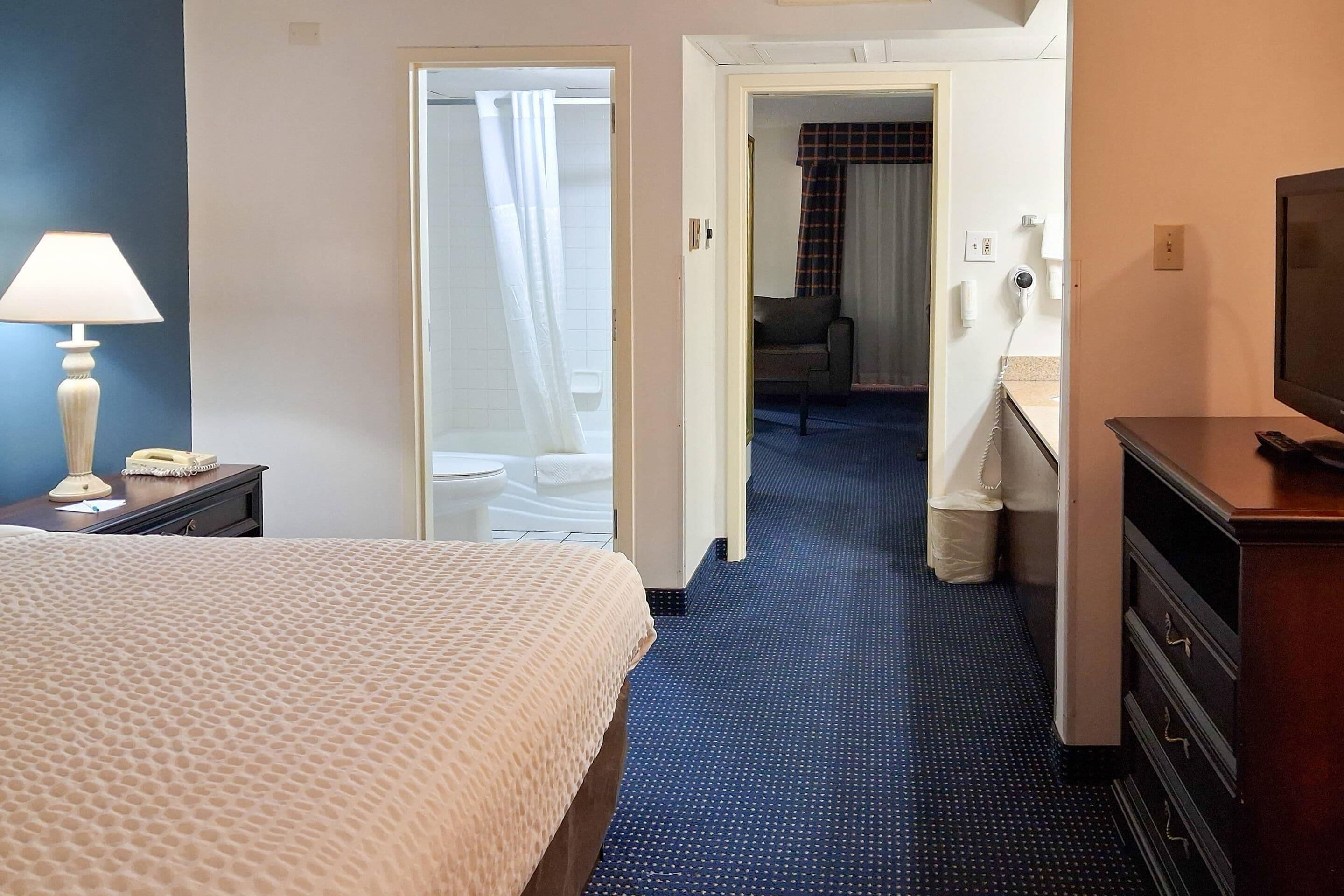 A hotel room with a bed, a desk, a chair, a television, and a bathroom visible through an open door.