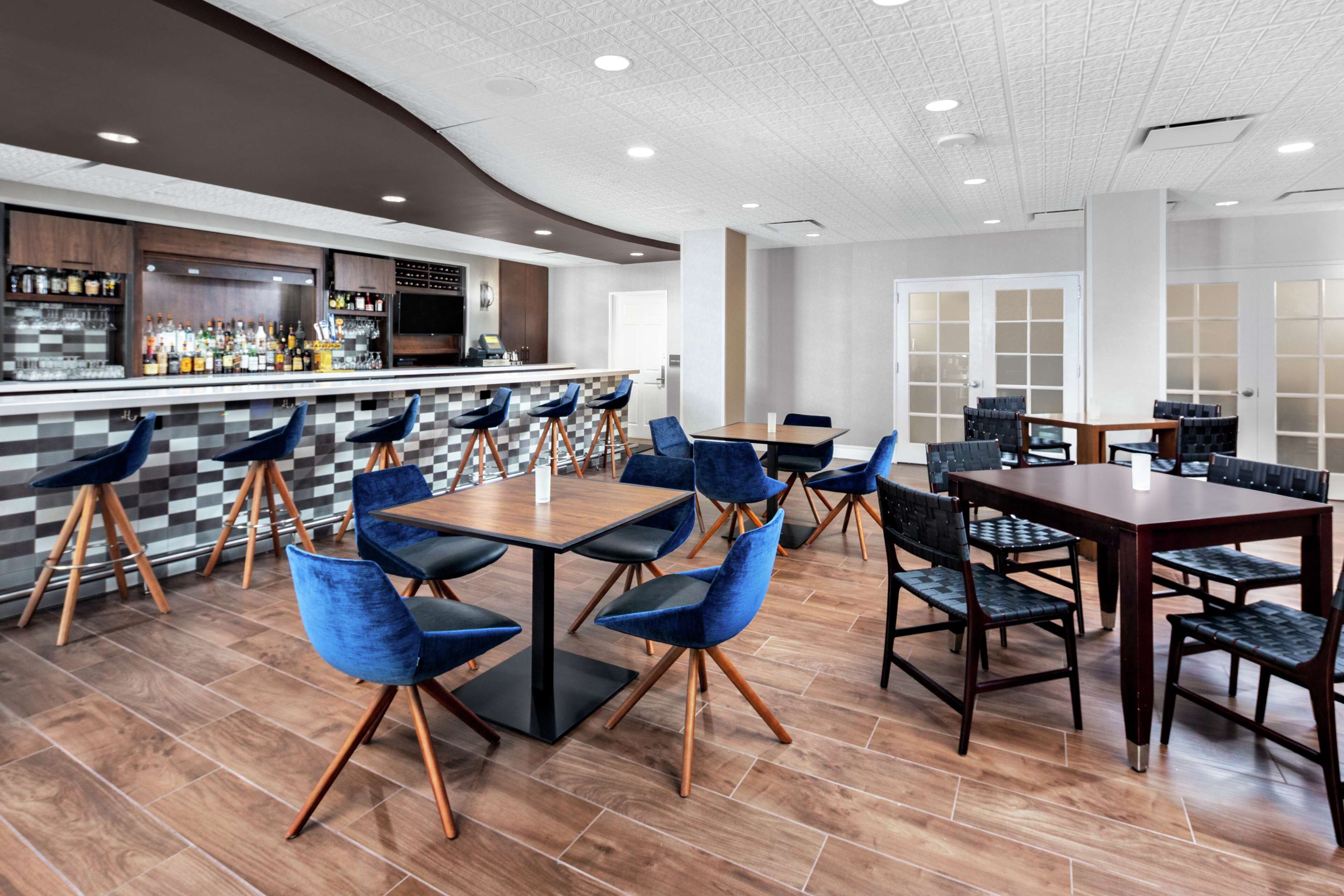 A modern restaurant with a bar area, multiple seating options including round tables and high chairs, and a checkered floor pattern.