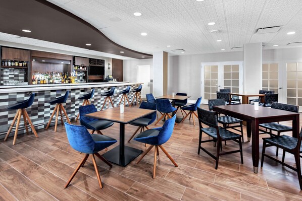 A modern restaurant with a bar area, multiple seating options including round tables and high chairs, and a checkered floor pattern.