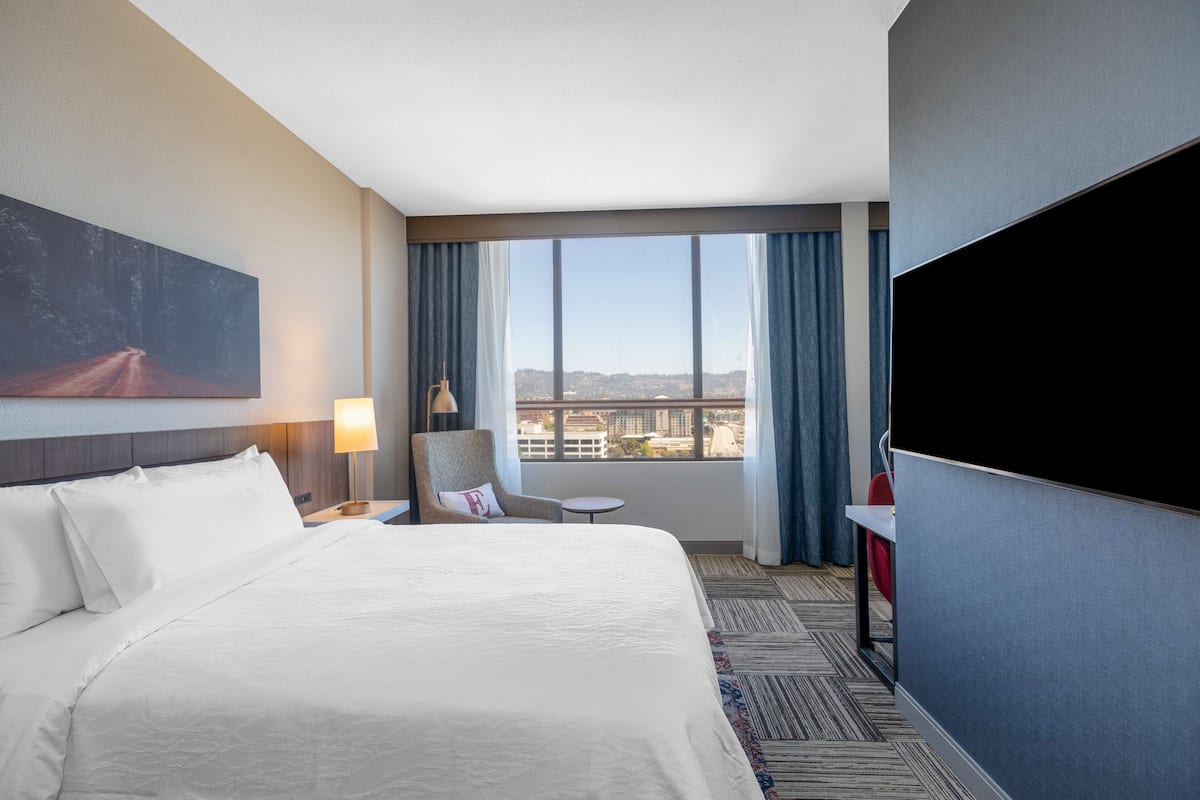 Une chambre d’hôtel avec un grand lit, un bureau, une chaise, une télévision et une fenêtre donnant sur la ville.