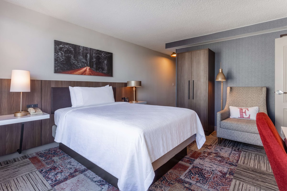 Une chambre d’hôtel avec un grand lit, une chaise, un bureau avec une lampe et un tableau au mur.
