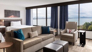 Une chambre d’hôtel comprenant un lit, un canapé, une chaise, une petite table et une vue sur un pont et sur l’eau.