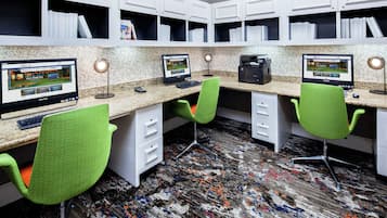 A modern office space with multiple desks, each equipped with a computer and a lamp. There are bookshelves above the desks, and the floor has a patterned carpet.