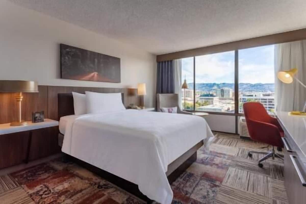 Een hotelkamer met een groot bed, een bureau, een stoel en uitzicht op de stad.