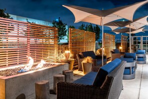 An outdoor seating area with wicker furniture, fire feature, and umbrellas.