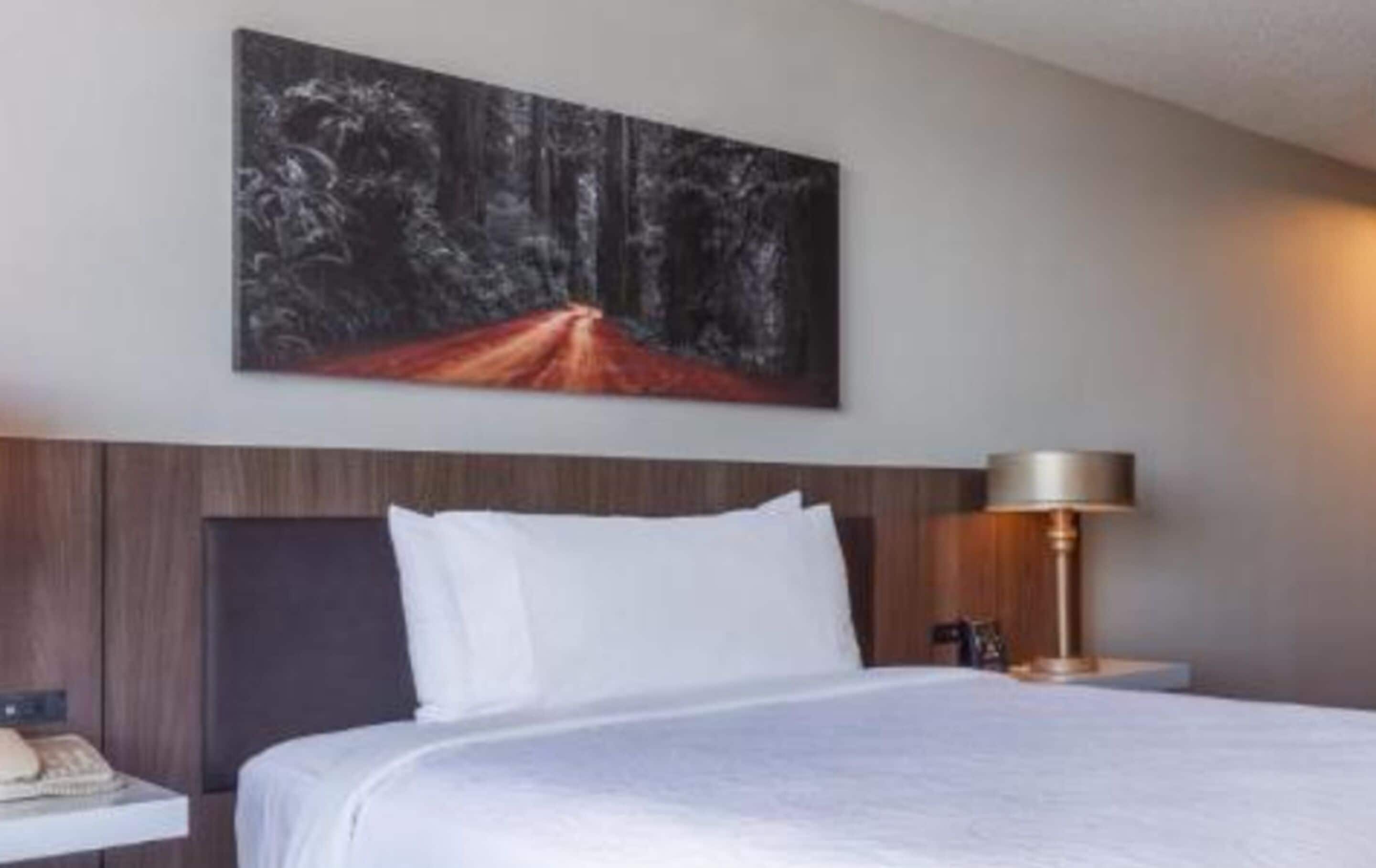 A hotel room with a large bed, a nightstand, a lamp, and a painting on the wall.