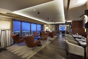 Habitación de hotel con vista a la ciudad, zona de comedor con mesas y sillas, y diseño de interiores moderno.