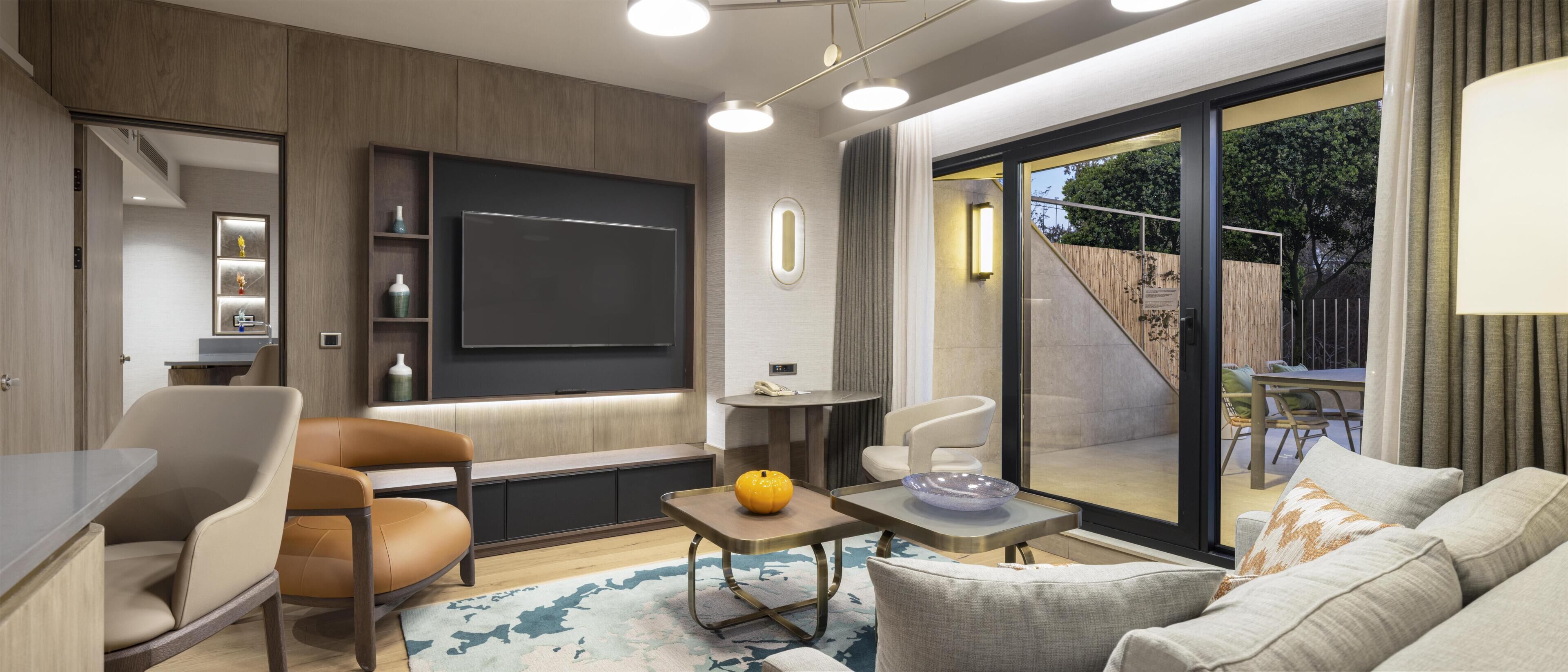 Una sala de estar moderna con televisión de pantalla plana, asientos cómodos, una pequeña mesa y vistas al exterior.