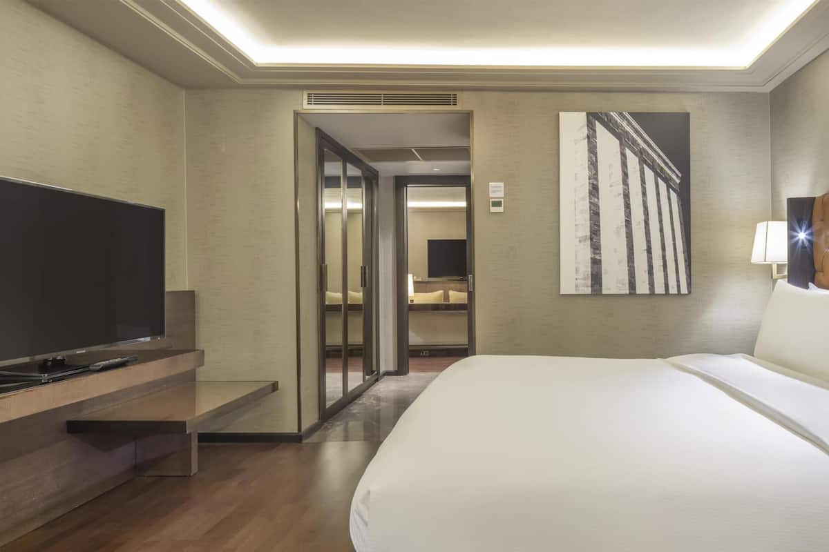 A hotel room with a large bed, a television on a wooden stand, a headboard with a tufted design, and a framed picture on the wall.