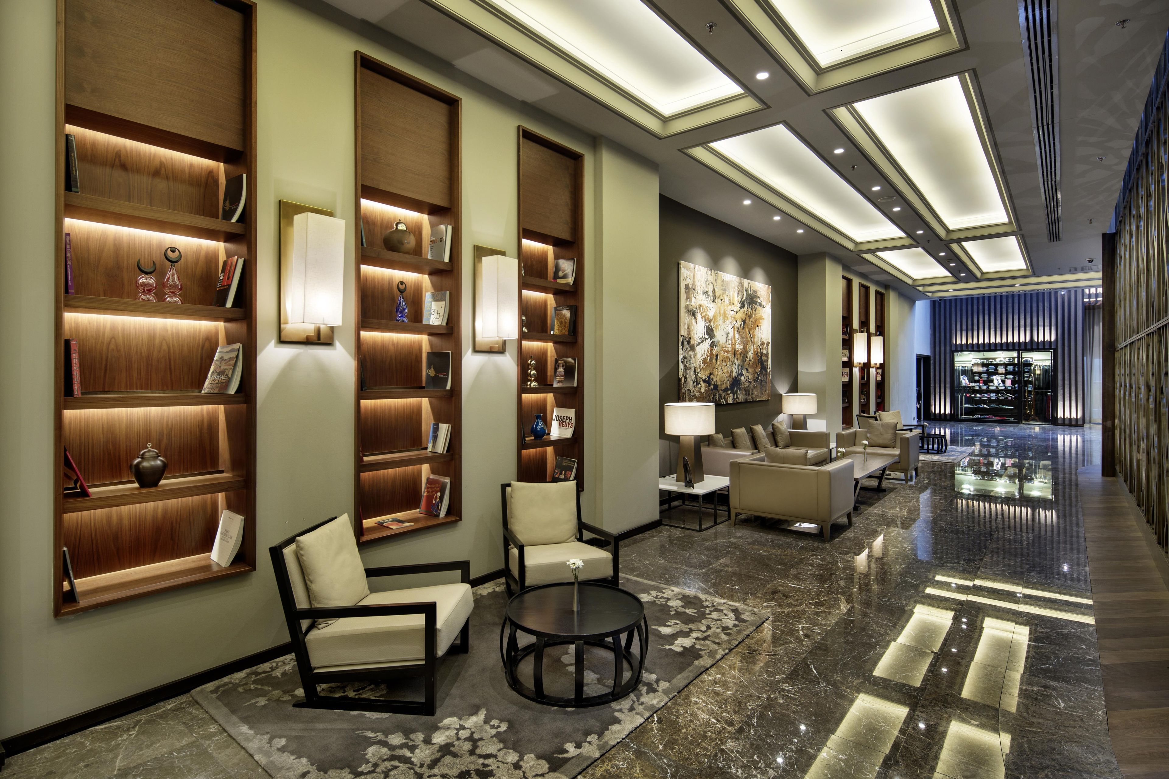 Een hotel lobby met een lange gang, houten boekenkasten, zithoeken en een groot abstract schilderij aan de muur.