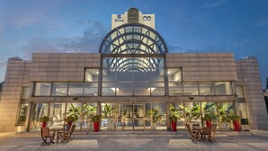 A hotel with a modern glass facade, a prominent logo at the top, and outdoor seating with potted plants. - Ankara HiltonSA (Ankara)