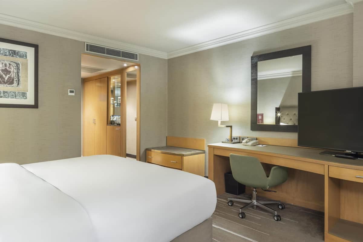 A hotel room with a bed, desk, television, and a framed artwork on the wall.