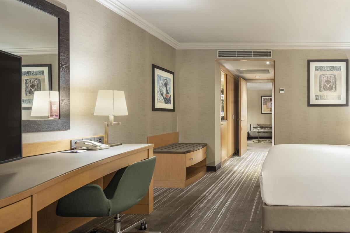 A hotel room with a bed, desk, chair, bedside table, and a large mirror.