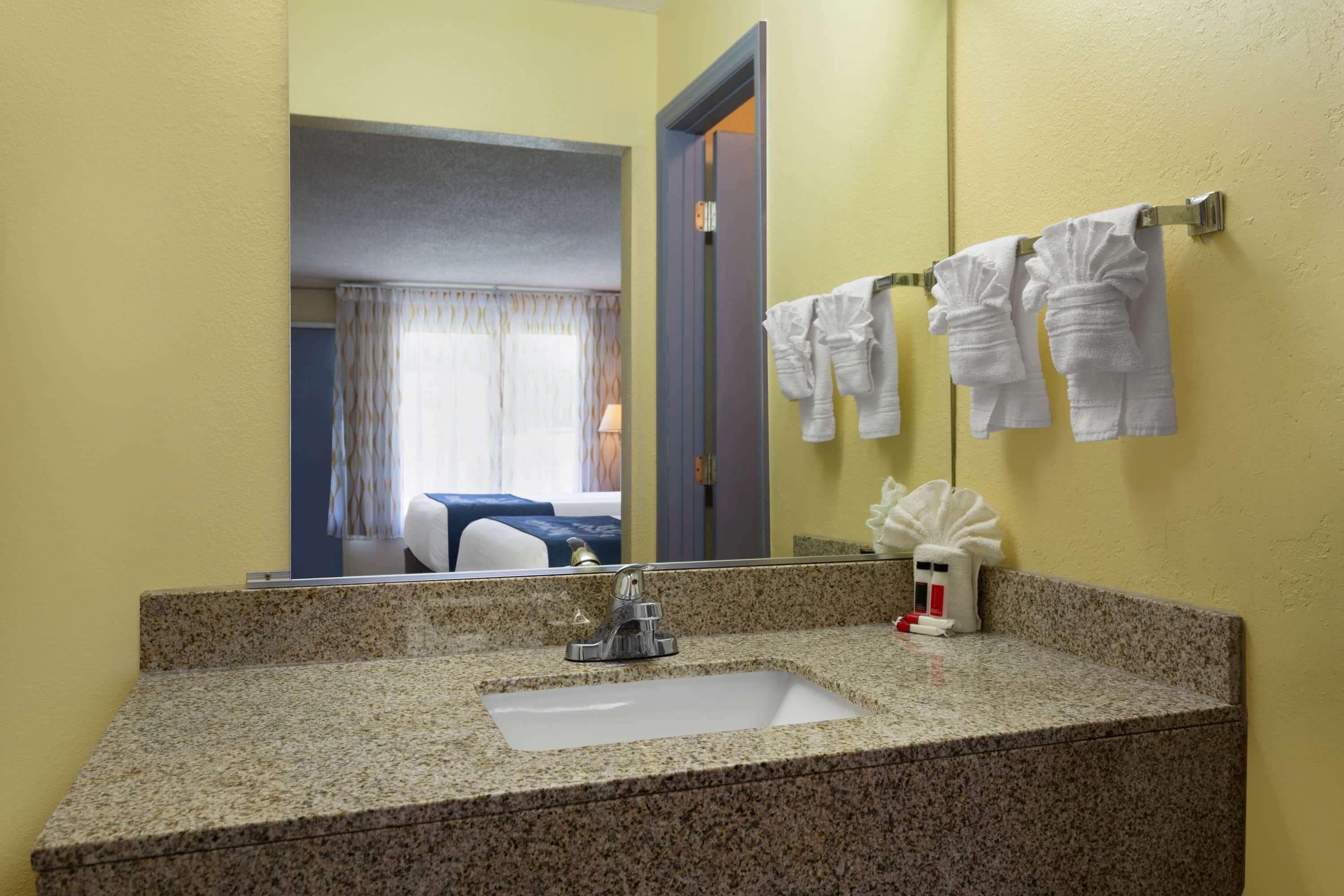 Un baño con encimera de granito, lavamanos, espejo y toallero con toallas.