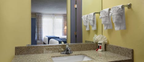 Un baño con encimera de granito, lavamanos, espejo y toallero con toallas.