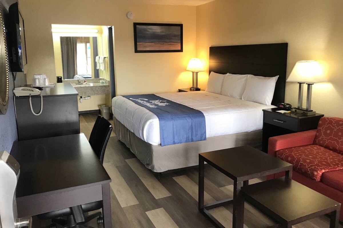 Habitació d'hotel amb un llit, dues làmpades de nit, escriptori, cadira, sofà vermell, taula petita, mirall, quadre a la paret i paperera.