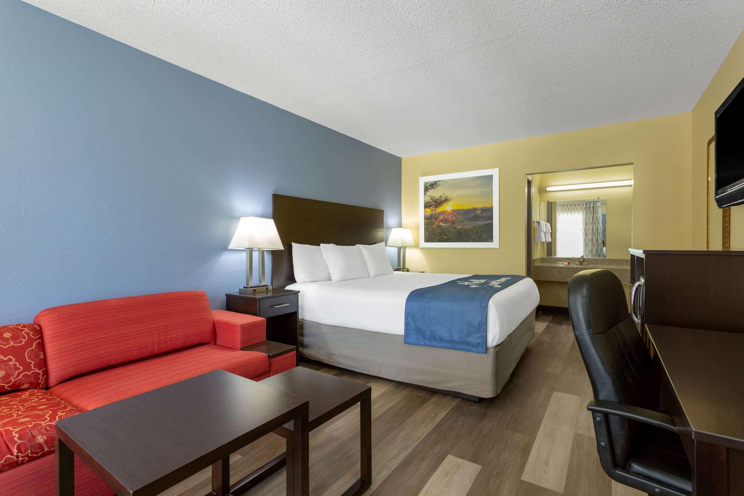 A hotel room with a bed, a red sofa, a desk, and a TV.