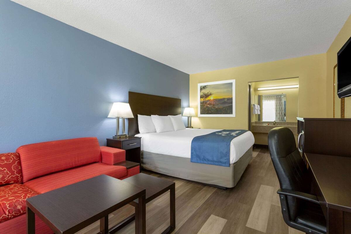 Habitació d'hotel amb un llit, un sofà vermell, una taula, una cadira i un quadre a la paret.