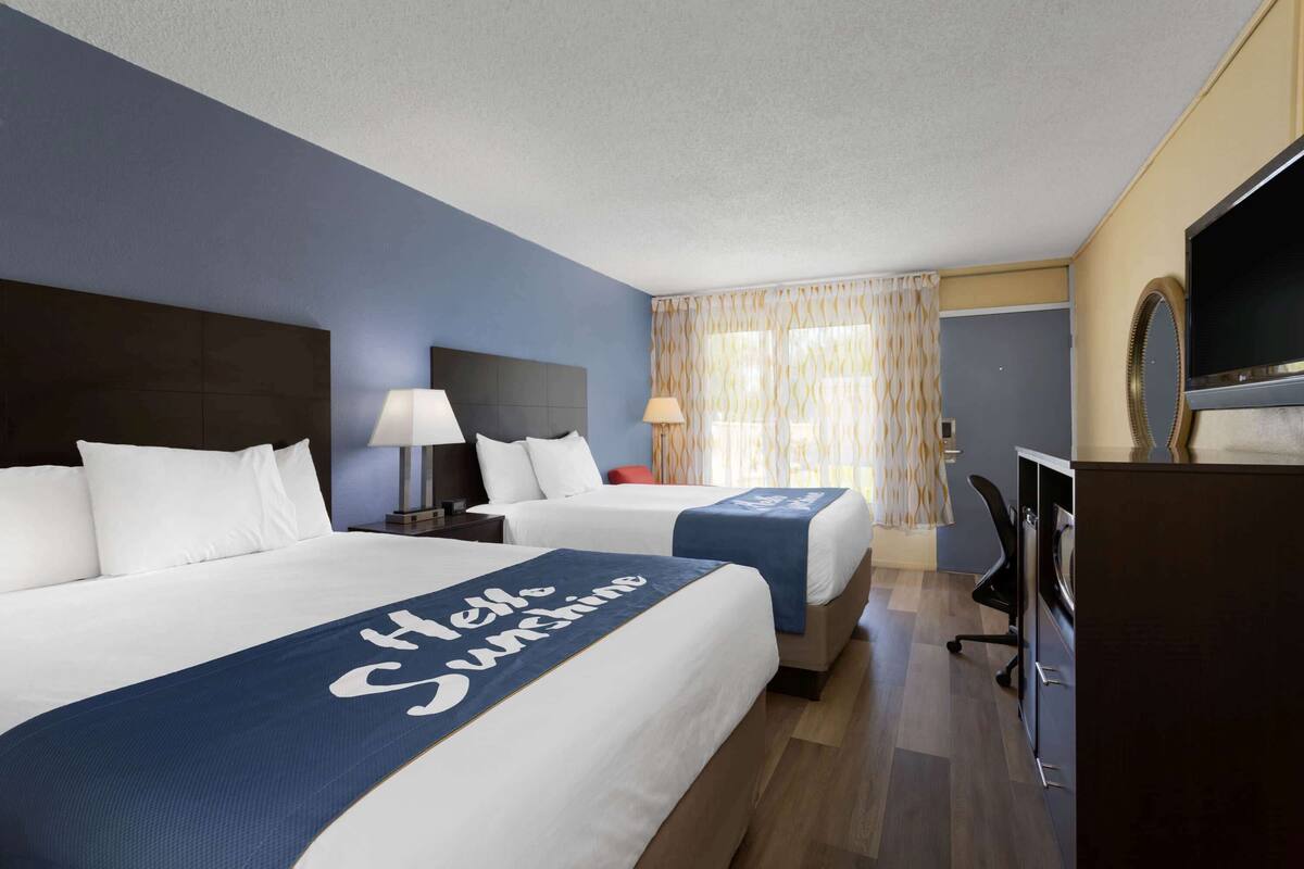 Habitació d'hotel amb dos llits, un escriptori, una televisió i un mirall.