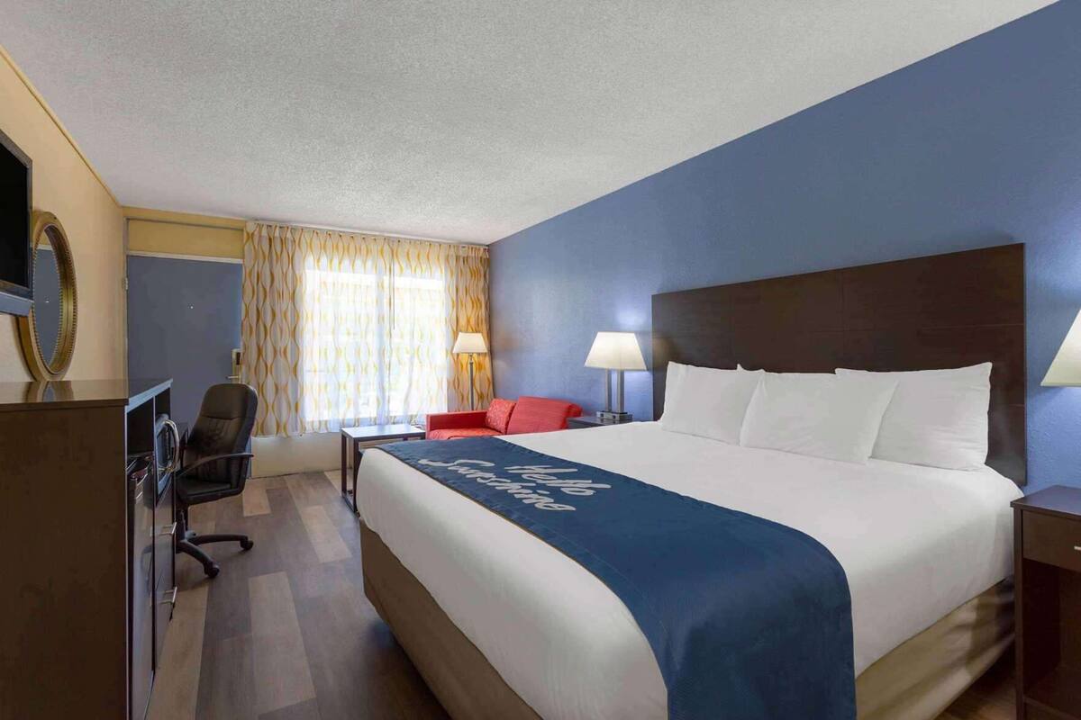 Habitació d'hotel amb un llit gran, escriptori, cadira, un sofà vermell i una làmpada.
