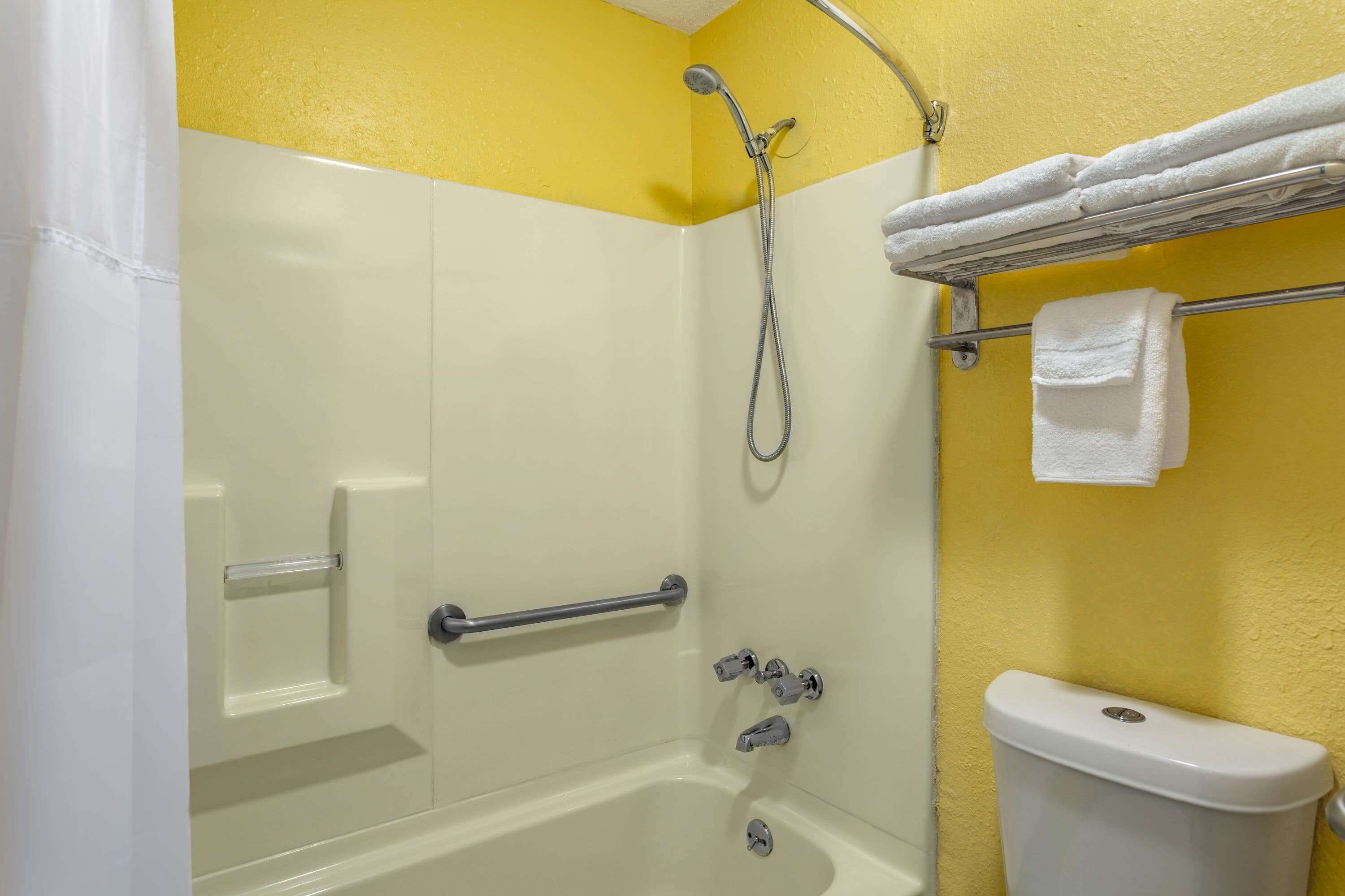 A bathroom with a bathtub, a shower, and a toilet. There is a towel rack with towels.