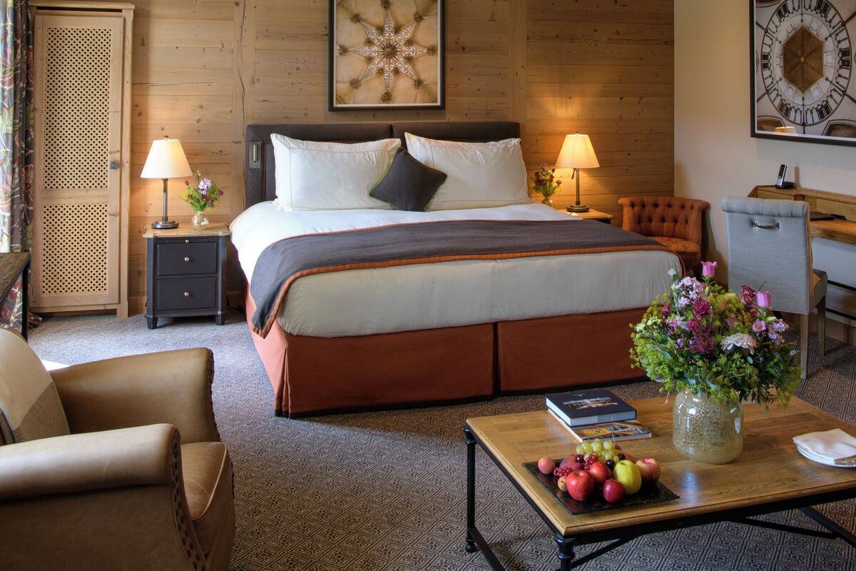 A bedroom with a large bed, wooden beams, a desk, and a chair.