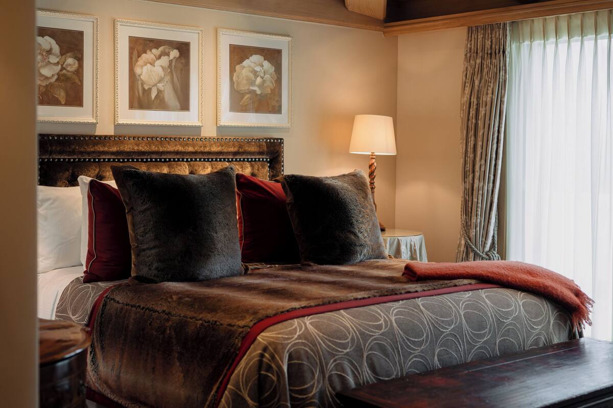 A bedroom with a large bed, a wooden headboard, a nightstand, a lamp, and a window with curtains.