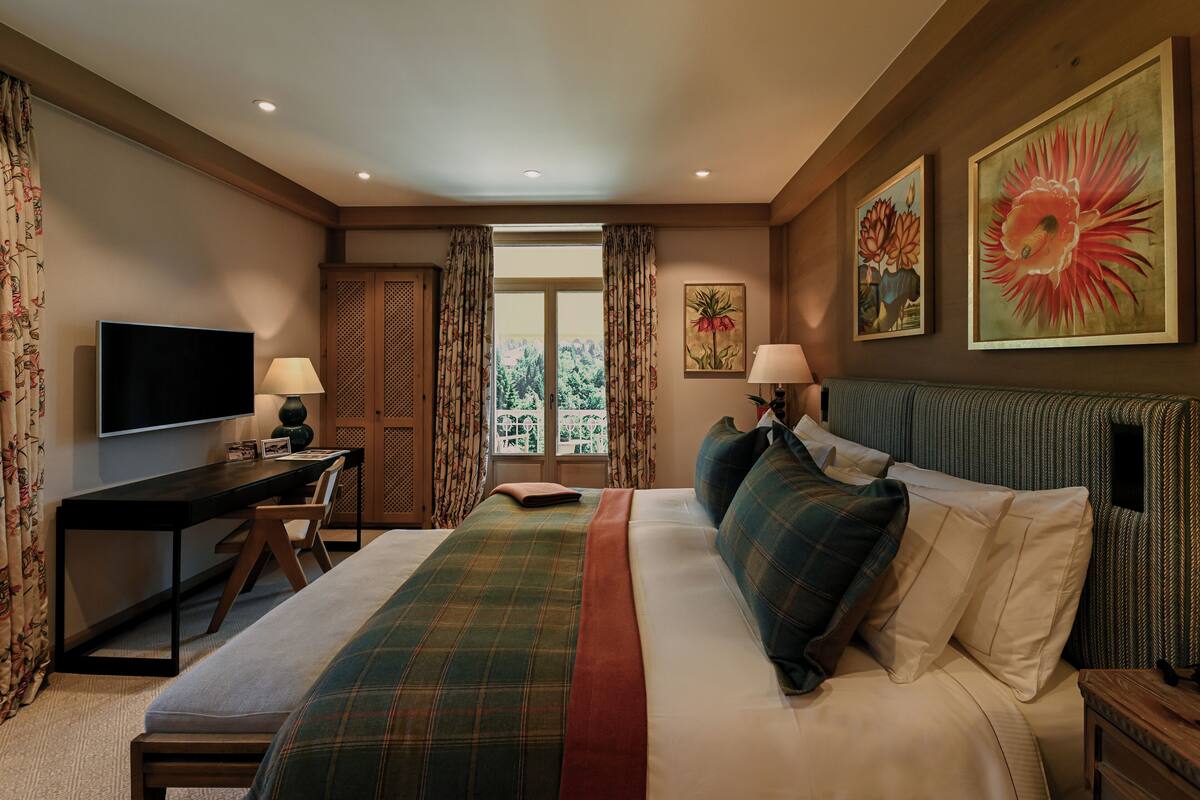 A hotel room with a bed, a desk, a television, and two paintings on the wall.