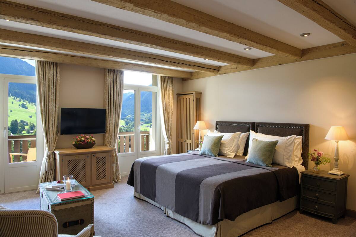 A bedroom with a large bed, a TV, a desk with a lamp, and a view of the outdoors.