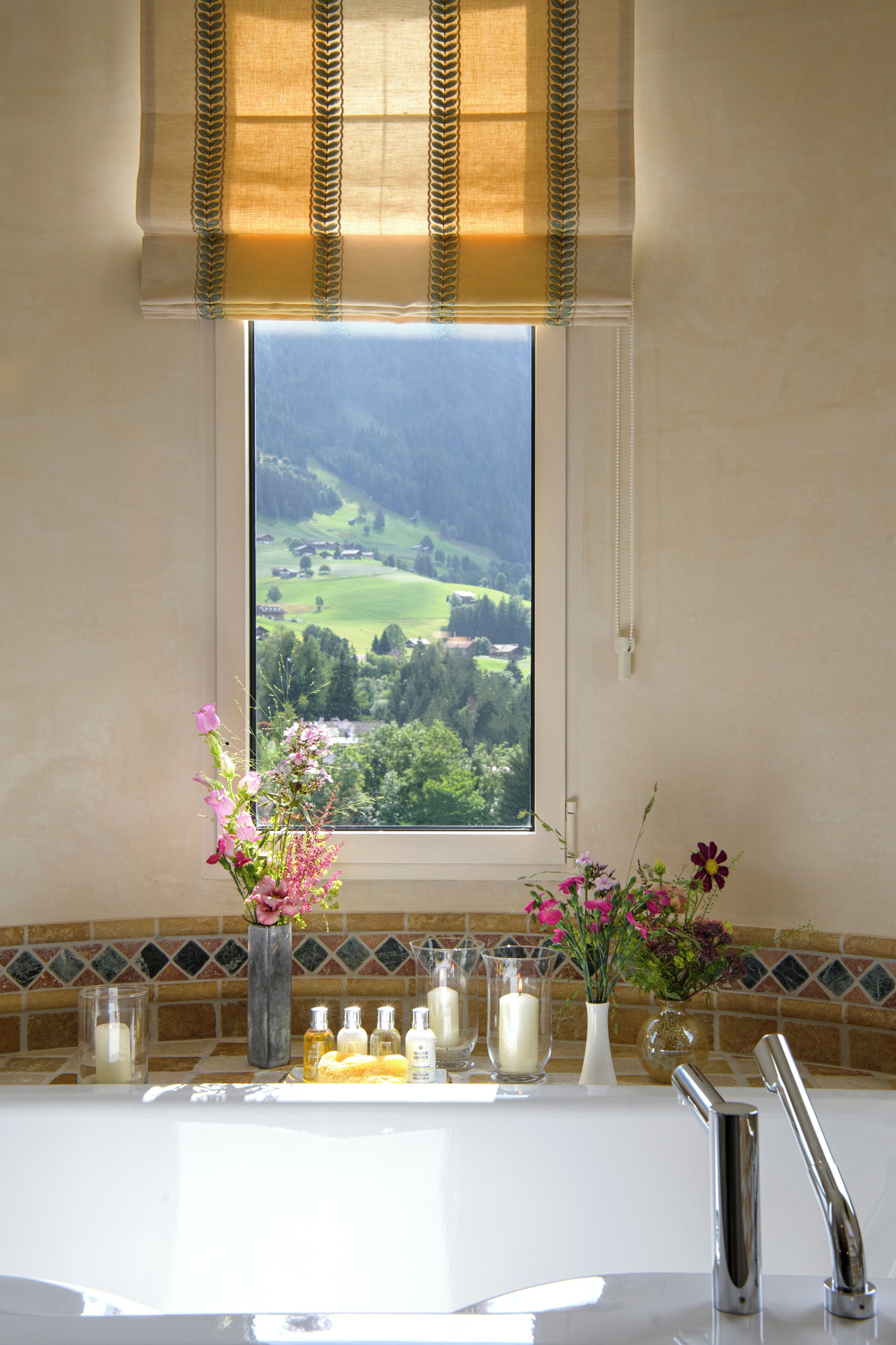 Une salle de bain avec une fenêtre donnant sur un paysage verdoyant, un lavabo avec des articles de toilette et un miroir.