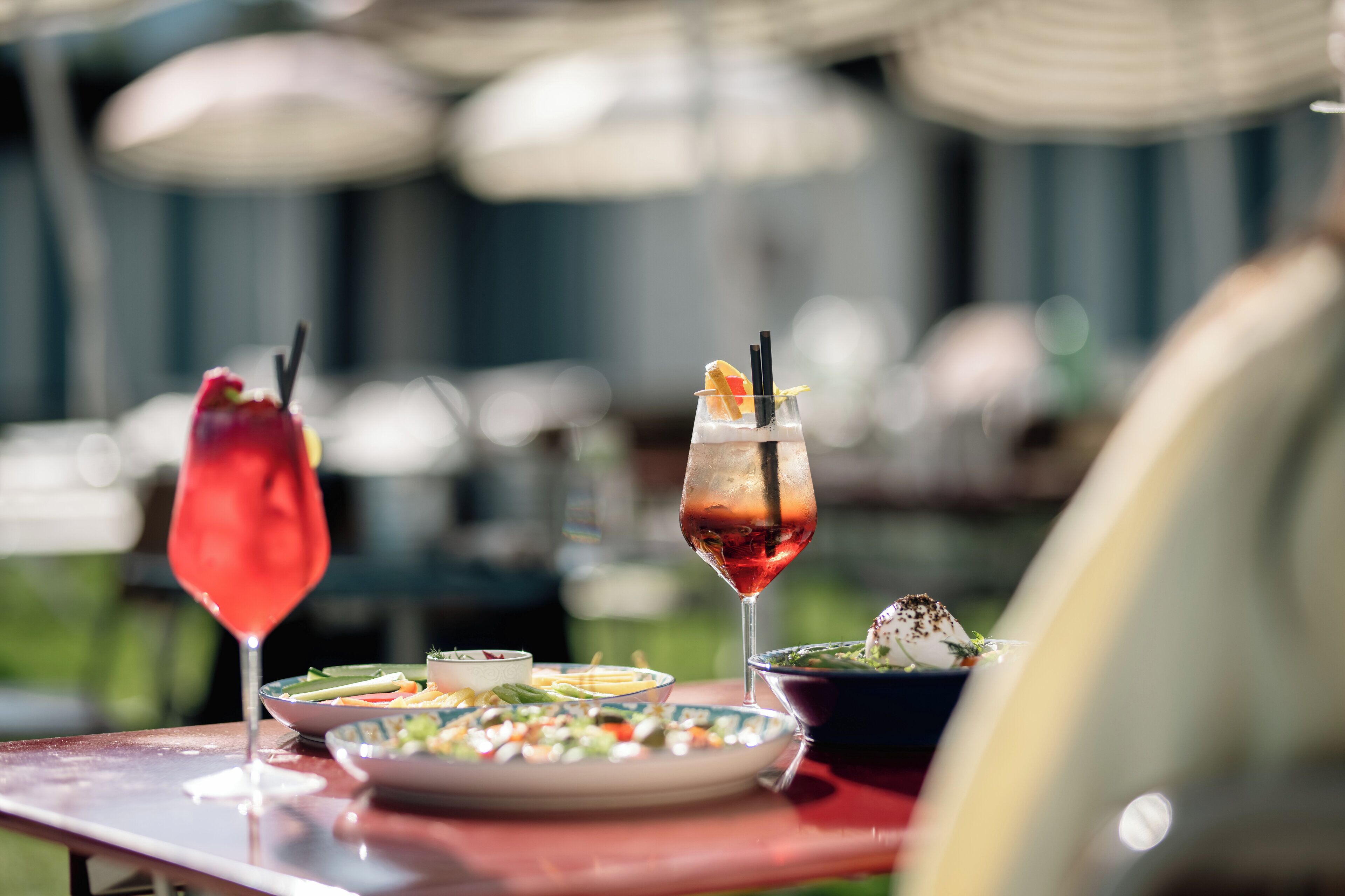 A table with a red drink, a glass with a red drink and a garnish, and a bowl of salad.