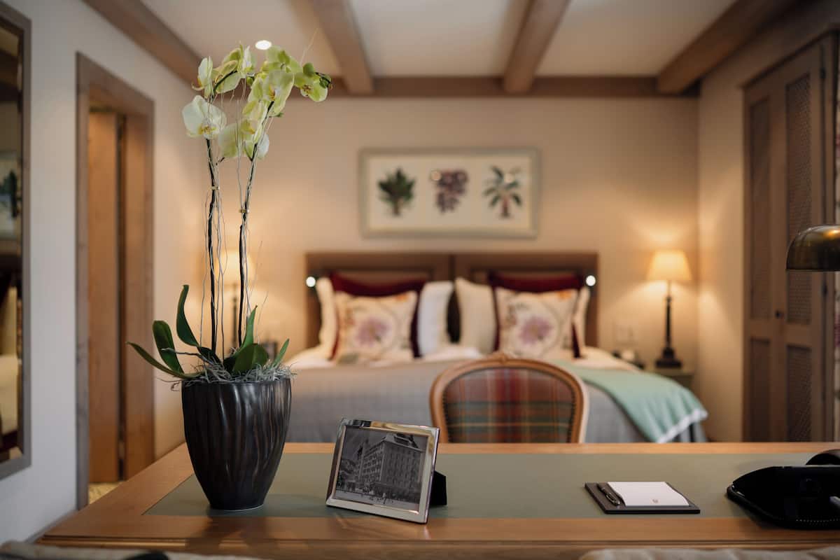A hotel room with a bed, a bedside table with a photo frame, a vase with orchids, and a lamp.
