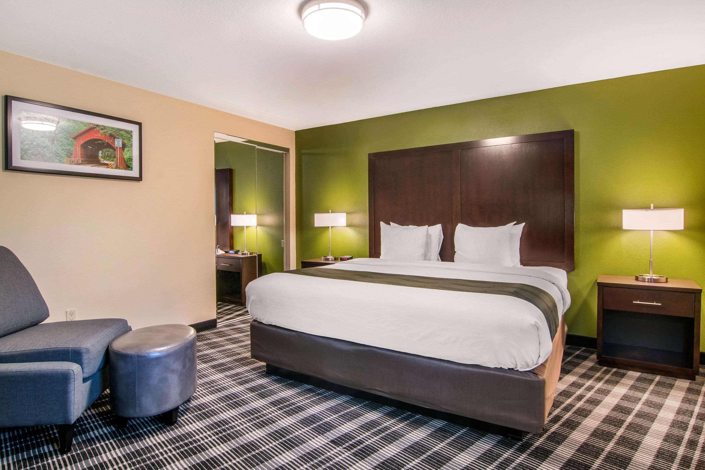 A hotel room with a large bed, a chair, a small table, and a nightstand.