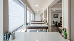 A modern hotel corridor with a long dining area, large windows, and a counter with condiments.