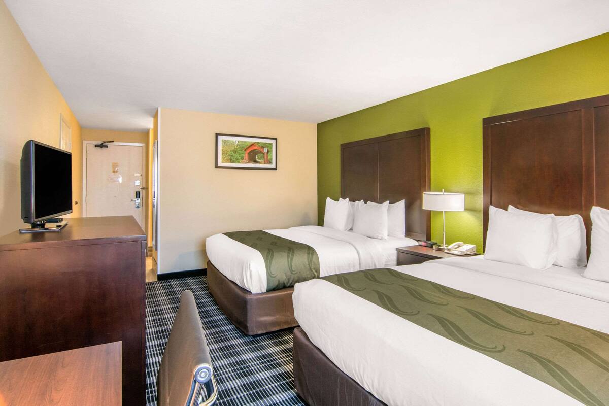 Habitación de hotel con dos camas, un escritorio, televisor y un cuadro en la pared.