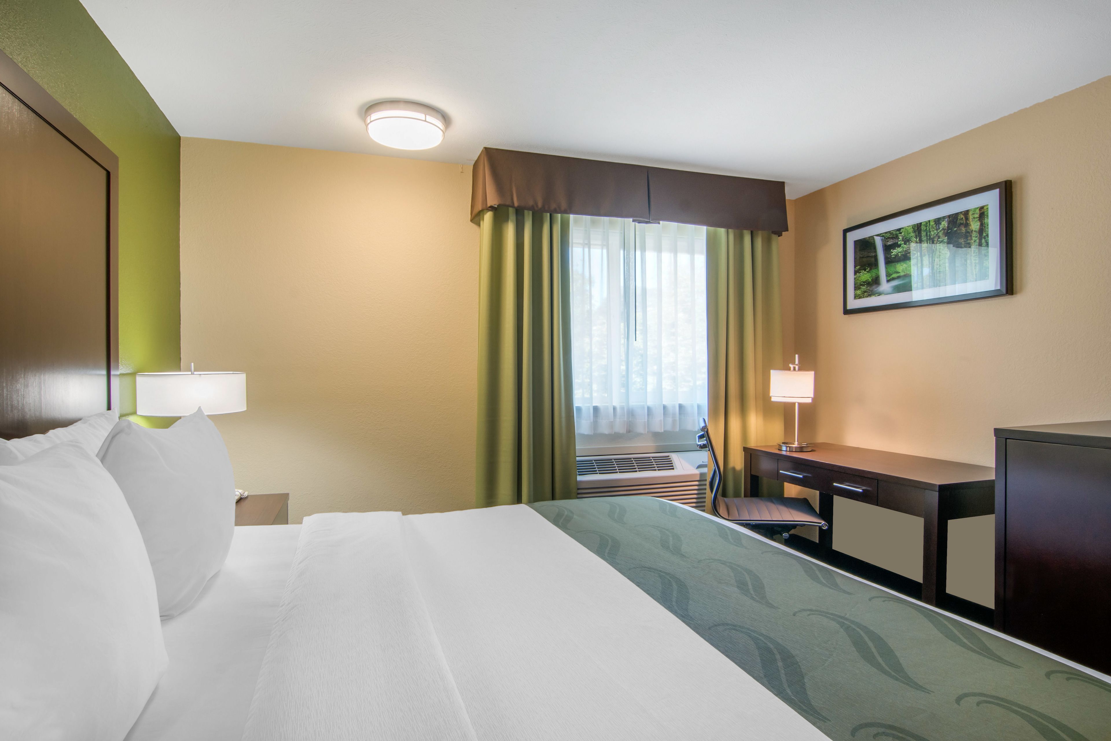 A hotel room with a bed, desk, chair, and a window with curtains.