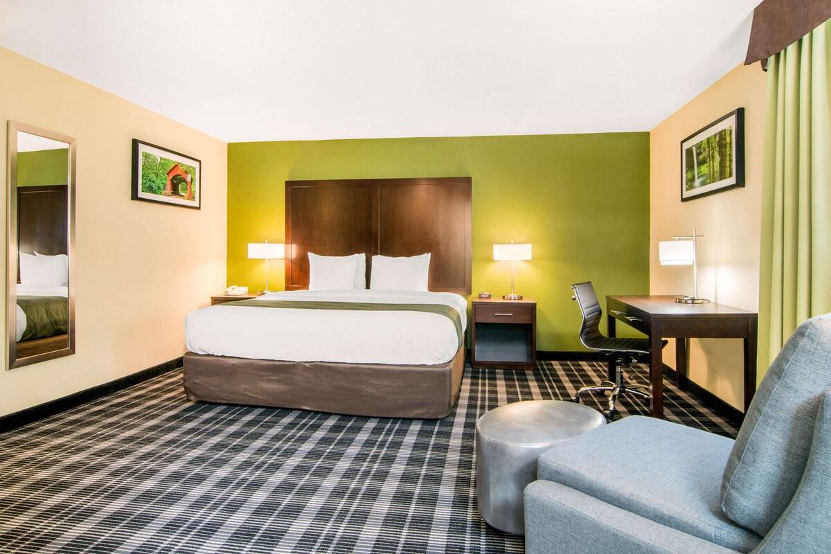 Una habitación de hotel con una cama grande, un escritorio, una silla y un pequeño reposapiés.