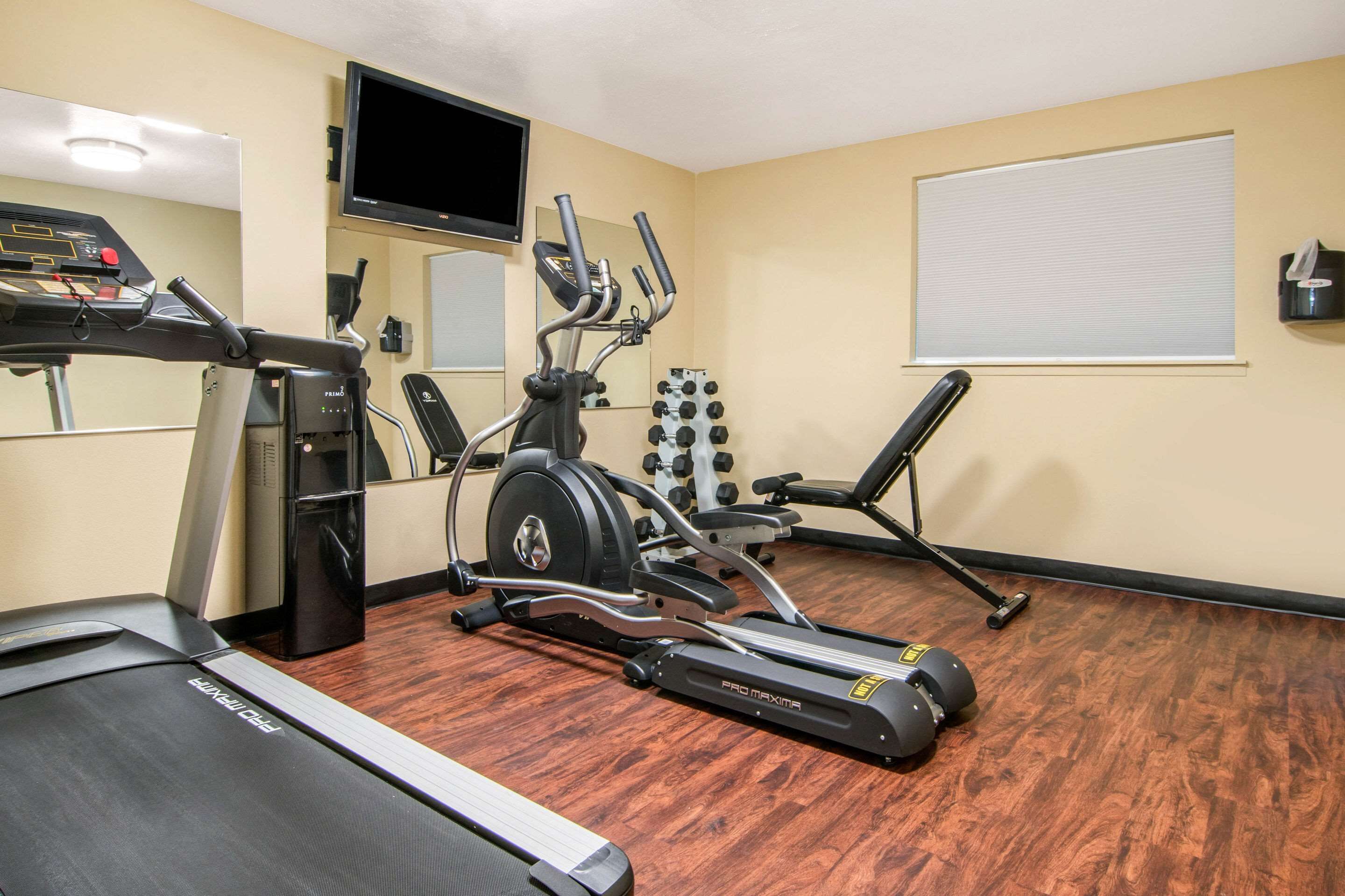 A gym with cardio equipment, a TV, and a mirror.