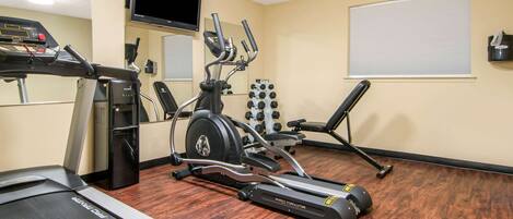 A gym with cardio equipment, a TV, and a mirror.