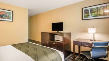 Habitación de hotel con cama, escritorio, silla, televisor, microondas y dos cuadros en las paredes.