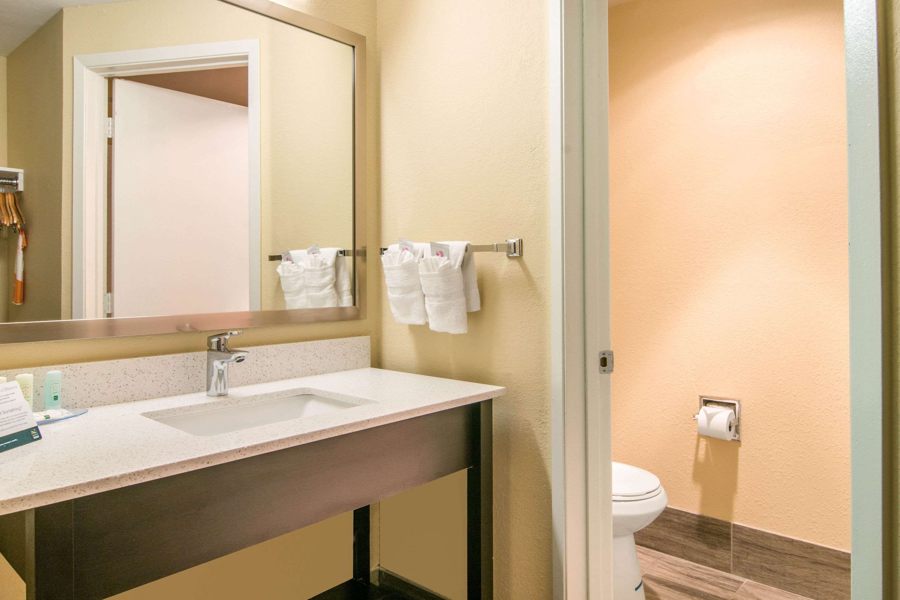 A hotel bathroom with a double sink, a mirror, a towel rack, and a toilet.