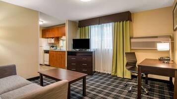 Une chambre d’hôtel équipée d’une kitchenette, d’une télévision, d’un bureau avec une lampe, d’une chaise et d’un canapé.