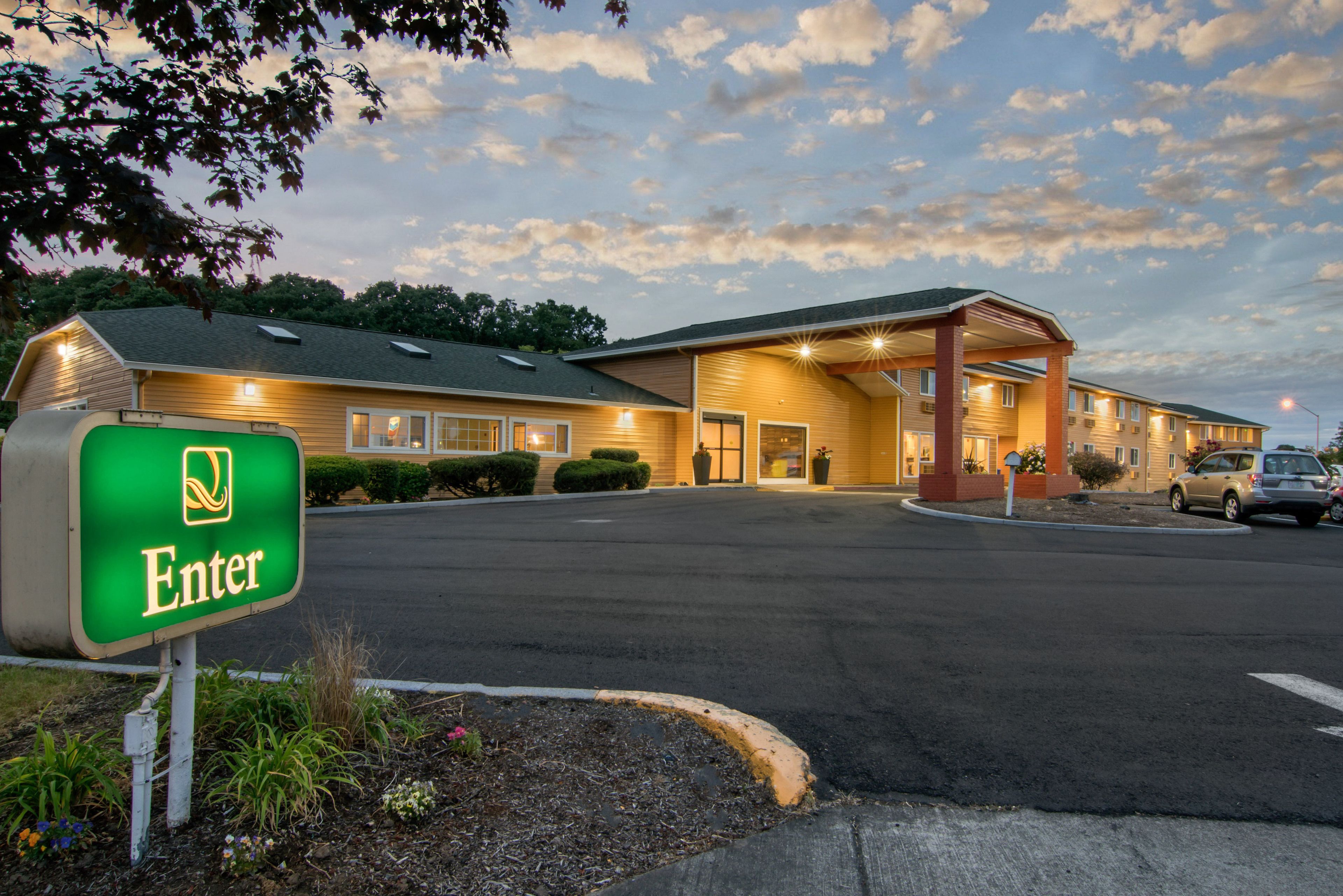 A hotel entrance with a green 'Enter' sign, a covered parking area, and a building with multiple windows and a roof.