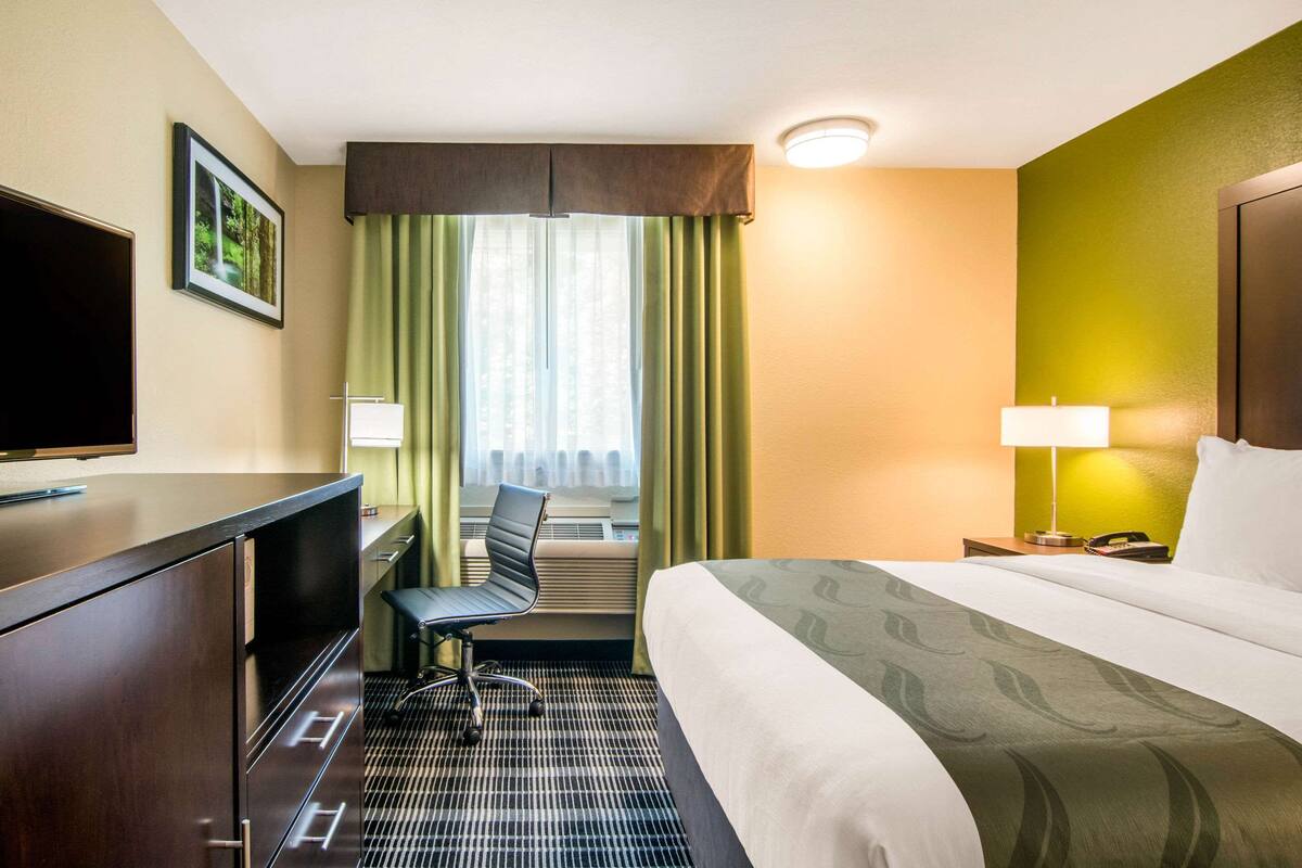 Habitación de hotel con cama, escritorio, silla y televisor.