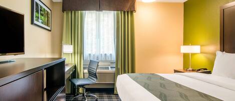 A hotel room with a bed, desk, chair, and a television.