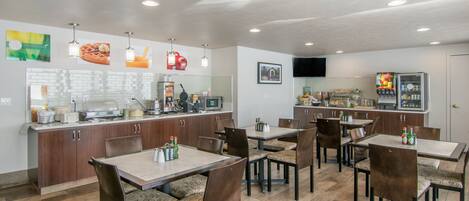 A modern restaurant with a kitchen area, dining tables, and chairs.