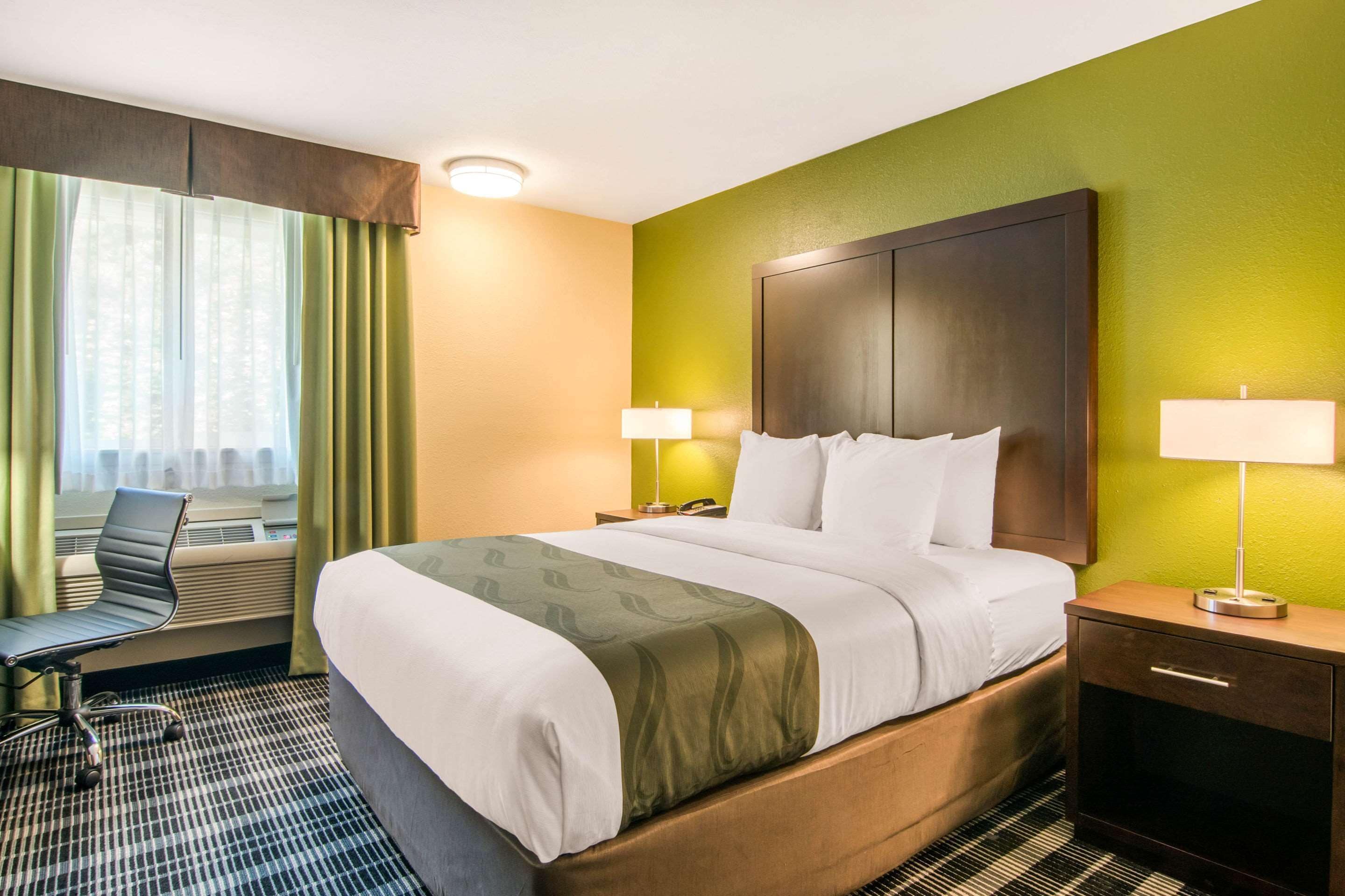 Habitación de hotel con una cama grande, dos lámparas de noche, un escritorio con silla y una ventana con cortinas.