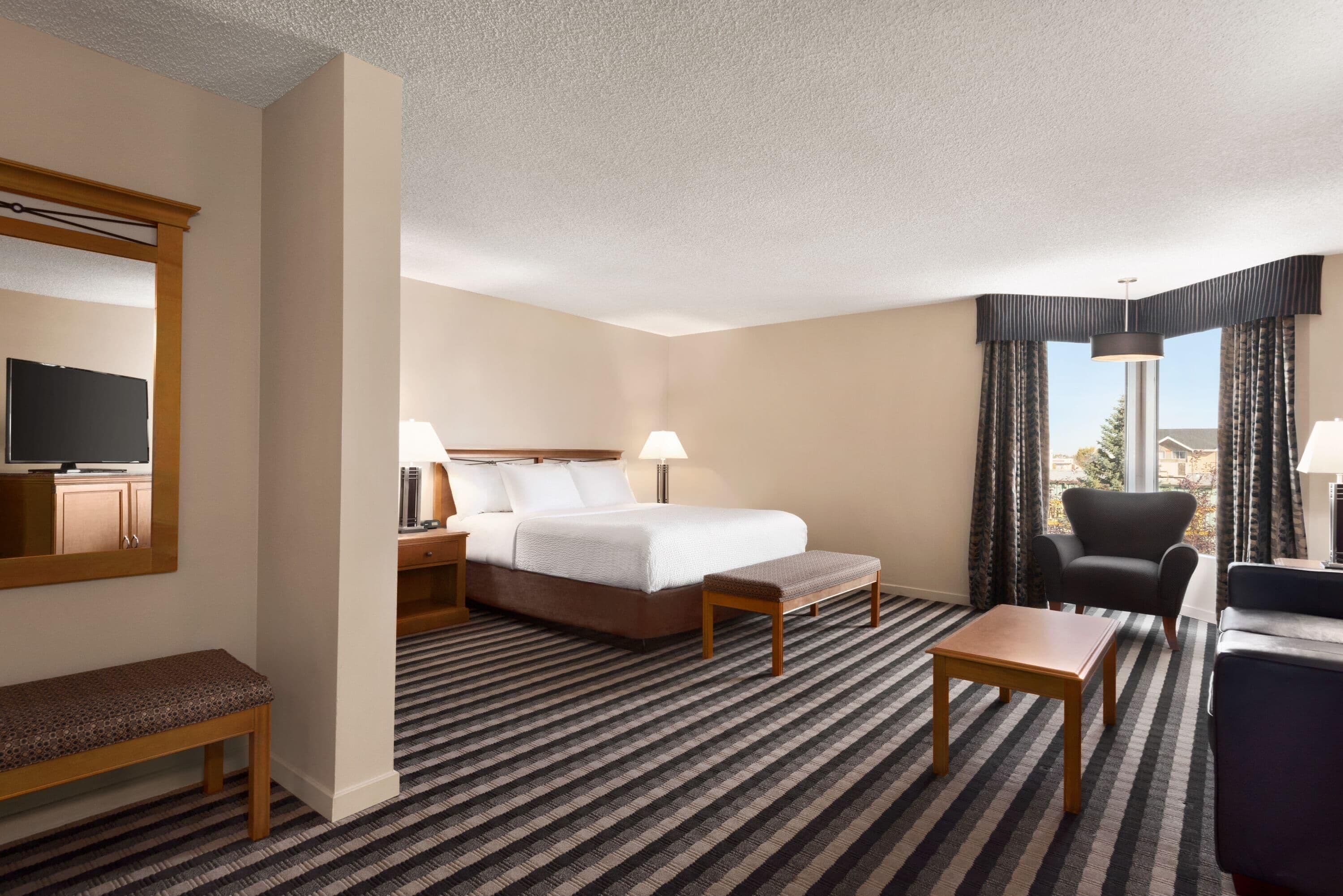Habitación de hotel con cama, mesitas de noche, un banco, escritorio, silla y televisión.