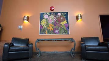 A lobby with two leather chairs, a bench, and a floral painting on the wall.